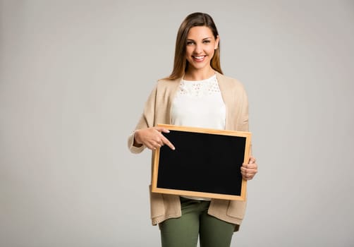 Beautiful and happy woman holding and pointing to a chalkboard
