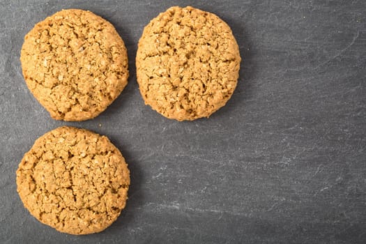 Three oatmeal cookies on a stone surface with copy space