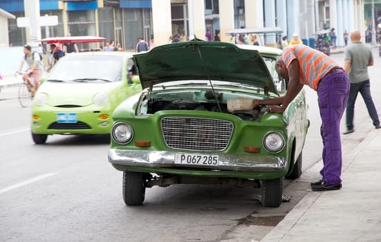 cuban man is putting the water into the radiator inside the old classic american car along the street at the Old Havana