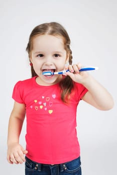 Little Smiling Girl Brushing Teeth.  Toddler Portrait on the gray
