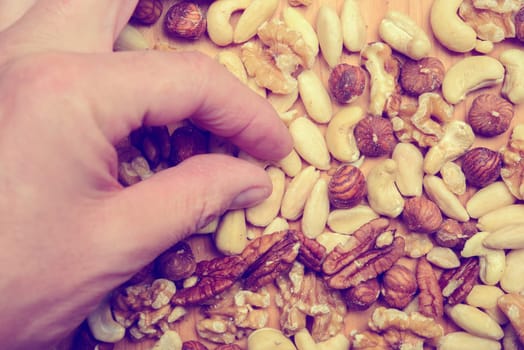 hand with different nuts on wooden ground from above
