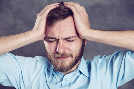 young bearded man in front of gray background has headache