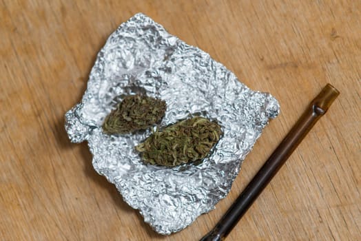 marijuana in tin foil with pipe on wooden table