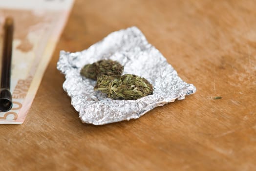 close up on marijuana in tin foil with pipe,euro money in background
