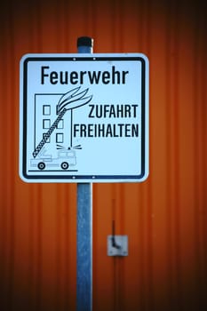 A sign for a fire brigade driveway in front of an abstract orange façade.