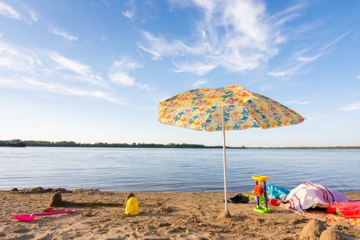Parasol on the river bank, under which the scattered items and toys