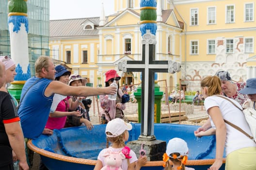 Sergiev Posad - August 10, 2015: Tourists are gaining the holy water in the passage of the bowl with a cross in Svvyato Trinity St. Sergius Lavra