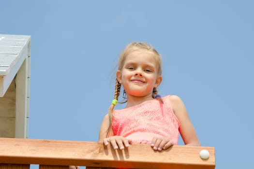 Happy girl climbed on the playground and looked down smiling