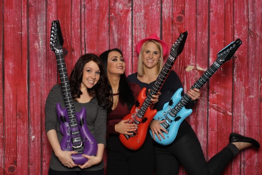 3 girls against a red background play on plastic guitars
