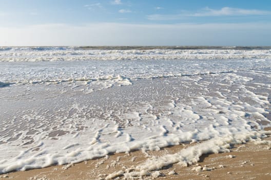 north sea beach full of foam on a windy spring day
