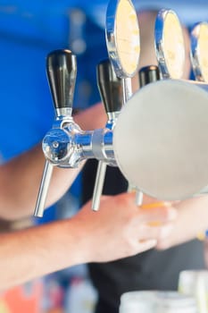 Barman hand at beer tap pouring a draught lager beer serving in a restaurant or pub.