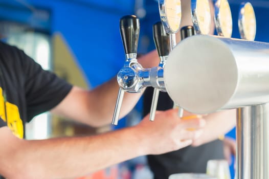 Barman hand at beer tap pouring a draught lager beer serving in a restaurant or pub.