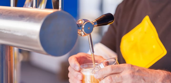 Barman hand at beer tap pouring a draught lager beer serving in a restaurant or pub.