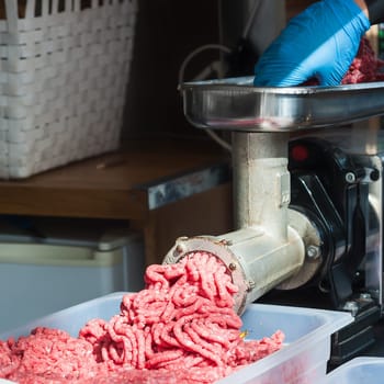 Tray of fresh minced meat. Butcher hand meat grinder and machine that puts the meat back into the machine.