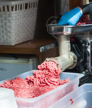 Tray of fresh minced meat. Butcher hand meat grinder and machine that puts the meat back into the machine.