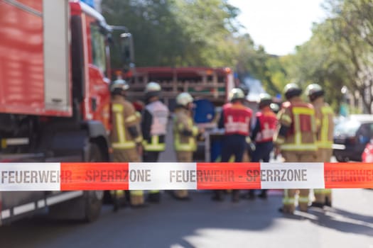 Team of blured firefighters by firetruck on protected accident site. Focus on red and white security band.