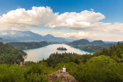 Relaxed female traveler enjoying beautiful panoramic view of Julian Alps, Lake Bled with St. Marys Church of the Assumption on the small island, Bled, Slovenia, Europe.