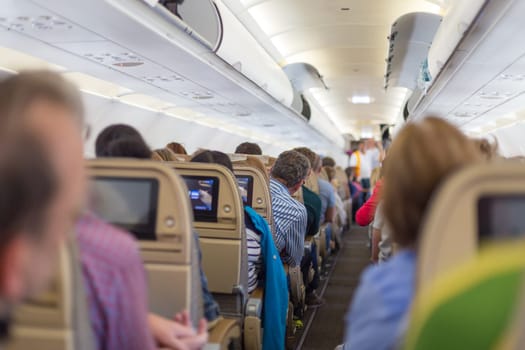 Interior of modern commercial airplane with passengers on their seats waiting to taik off.