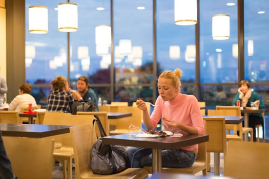 Young female traveler eating pizza at airport restaurant while waiting for late night flight departure.