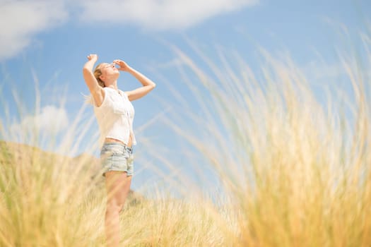 Relaxed woman, arms raised, enjoying sun, freedom and life an a beautiful beach. Young lady feeling free, relaxed and happy. Concept of vacations, freedom, happiness, enjoyment and well being.