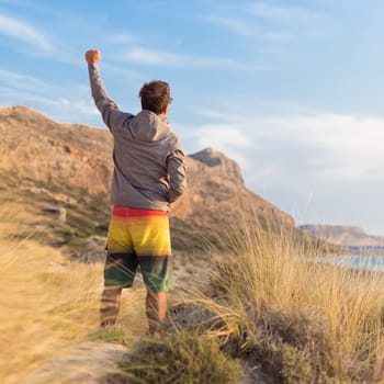 Sporty active man, arm raised, enjoying beauty of nature, freedom and life at beautiful landscape. Active lifestyle outdoors. Made it.