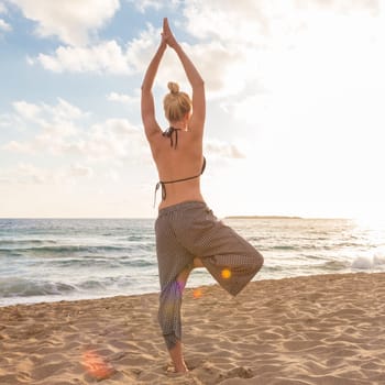 Active young woman practicing yoga on beach at sunset.