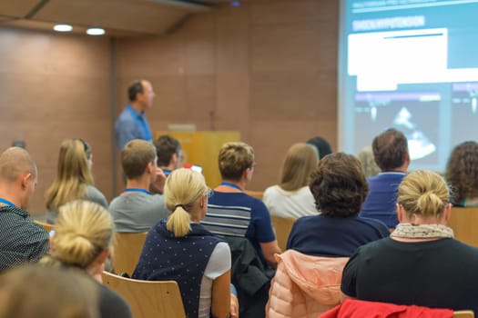 Speaker Giving a Talk at Business Meeting. Audience in the conference hall. Business and Entrepreneurship. Focus on unrecognizable people from rear.
