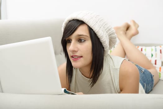 young brunette girl student lying on the couch with a laptop