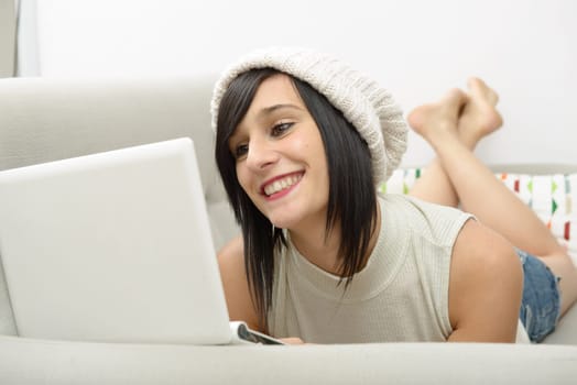 young brunette girl student lying on the couch with a laptop
