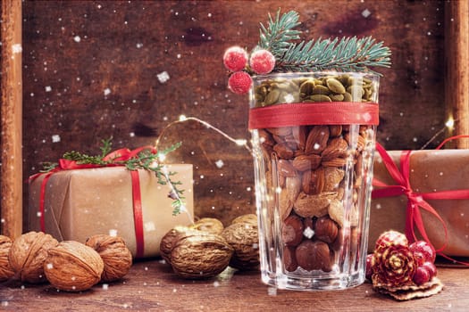 Christmas decoration glass with a variety of nuts on a wooden background with flying snow and copy space