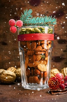Christmas decoration glass with a variety of nuts on a wooden background with flying snow