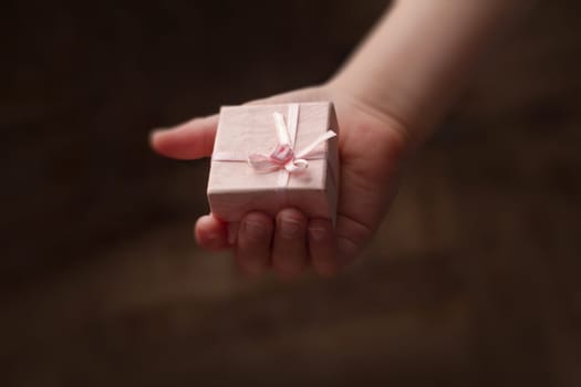 Horizontal top view hand of a child holding a small pink gift box on dark background