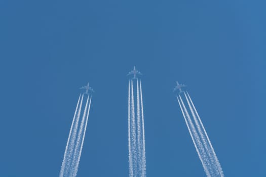 Three planes flying at high altitude. Contrails against a dark blue sky.