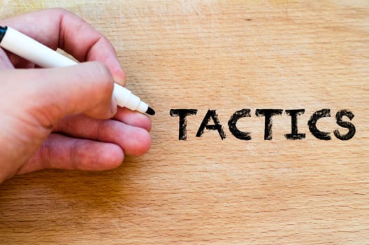 Human hand over wooden background and tactics text concept