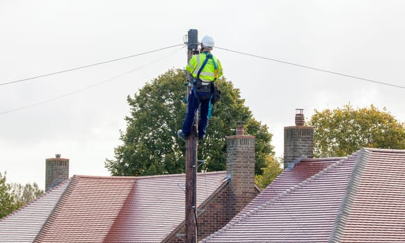 FAKENHAM, NORFOLK / UK - 10th OCTOBER 2016: Openreach BT engineer fixing cables up a pole. UK internet and telephone infrastructure provider at work providing internet and telephone services to rural locations
