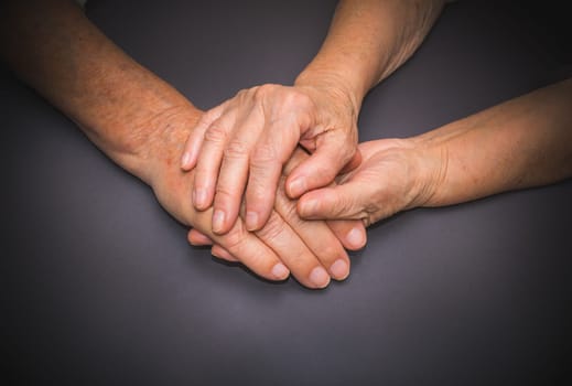 Hands of two loving senior people on a gray dark background