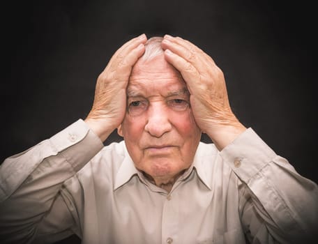 Portrait of an elderly man with face closed by hands on black