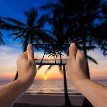 Nice sunset. Tropical sunset, palm trees. Hand with a smartphone. Taking photo