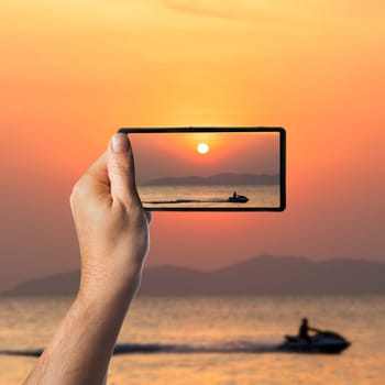 Nice sunset. Hand with a smartphone. Taking photo