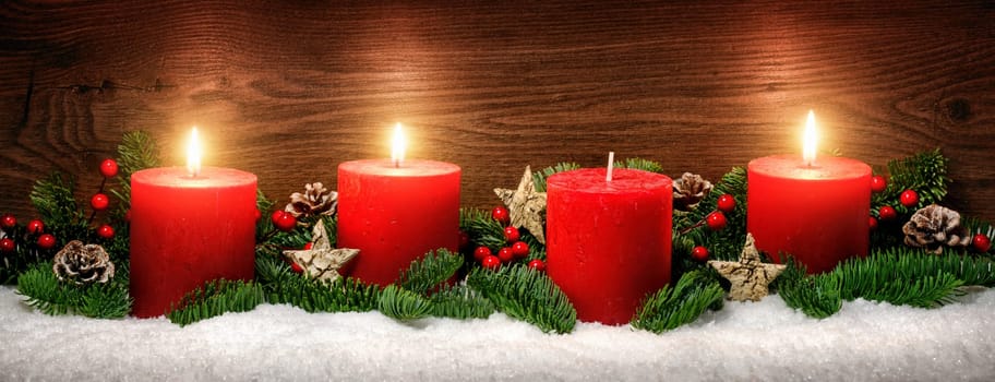 Low-key studio shot of elegant advent decoration with fir branches on snow and three burning red candles,dark wood background