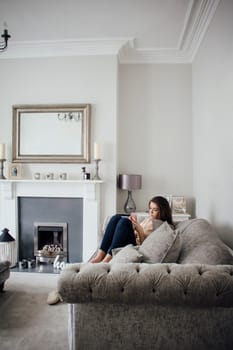 Teenage girl sitting on the sofa in her home, using a smart phone.