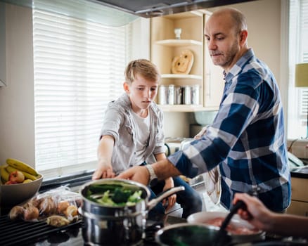 Father and son cooking dinner together in the kitchen. They are cooking vegetables on the hob.