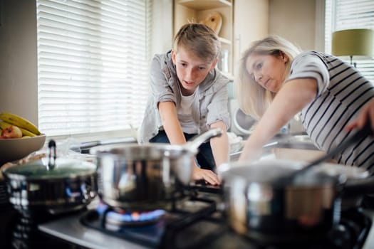 Mother and son cooking dinner together in the kitchen. They are cooking vegetables on the hob.