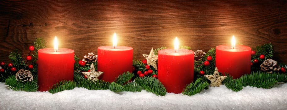 Low-key studio shot of elegant advent decoration with fir branches on snow and three burning red candles,dark wood background