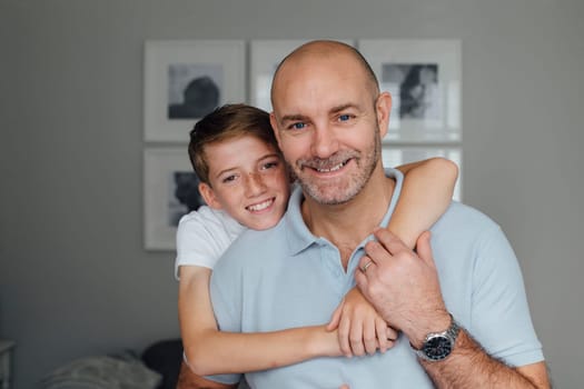 Father and son posing for the camera. The boy has his arms around his father and is leaning over his shoulder.