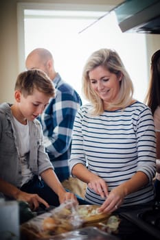 Family in the kitchen preparing food. The mother and her son are helping each other to cut up onions on a chopping board.