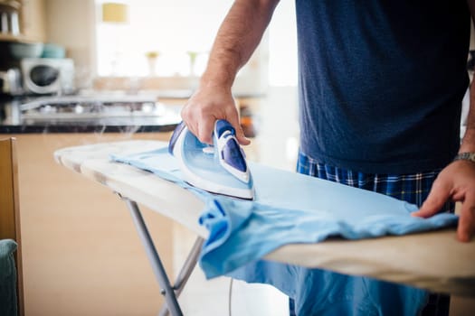 Close up of a mature man ironing a t-shirt in the kitchen.