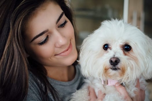 Close up of teenage girl with her pet Bichon Frise. The girl is looking at her dog and smiling.
