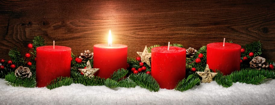 Low-key studio shot of elegant advent decoration with fir branches on snow and one burning red candle,dark wood background