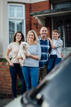 Family standing outside their home together with their pet dog, smiling for the camera.